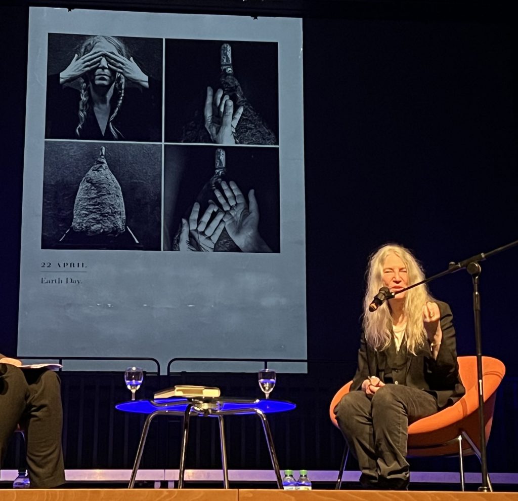 Patti Smith im Gespräch auf der Bühne der Universität Köln. Im Hintergrund in Groß, der Eintrag vom 22. April zum Tag der Erde im BUCH DER TAGE