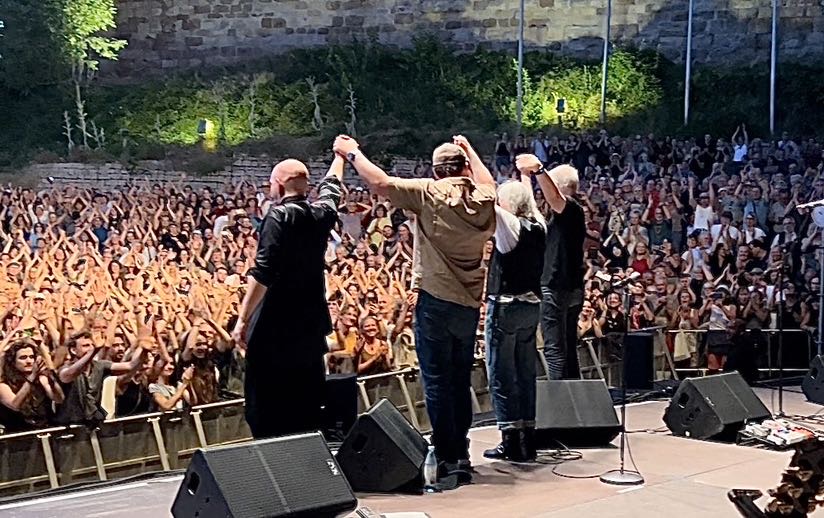 Patti Smith und ihr Quartett am Ende des Konzerts auf der Burg Abendberg. Das Bild wurde von der Bühne aus aufgenommen von Janine Bub und zeigt die Band von Hinten, die Hände nach oben gestreckt und aneinander haltend.