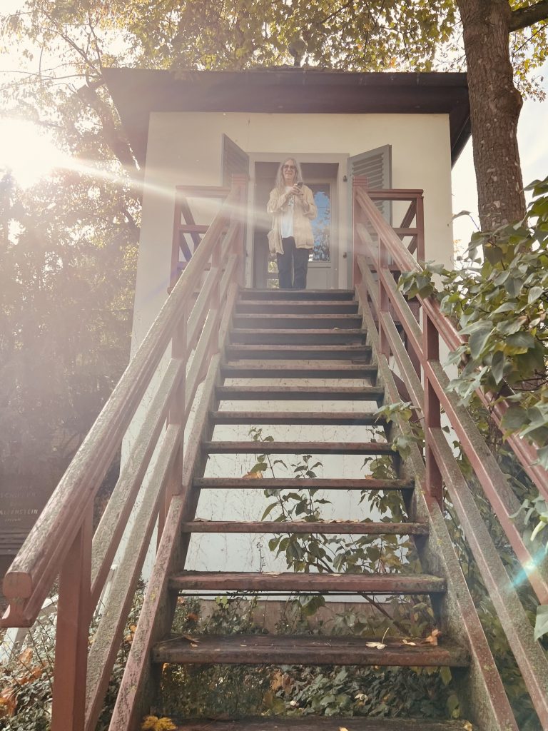 Bild von Patti Smith Besuch in Schillers magischem Garten in Jena, Deutschland im Oktober 2023. Das Bild zeigt Patti Smith aus der Gartenzinne Schillers kommend, kurz bevor sie die Holztreppe hinunter geht.