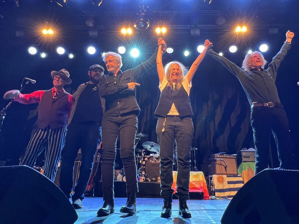 Patti Smith feiert ihren Geburtstag im Brooklyn Steel am 30. Dezember 2022. Das Bild ist vom Ende des Konzerts. Alle stehen nebeneinander in der Mitte der Bühne. Patti mittig, rechts daneben Lenny Kaye. Links neben ihr stehen Tony Shanahan, Jackson Smith und Jay Dee Daugherty. Das Bild wurde während ihrer Verneigung vor dem Publikum aufgenommen.