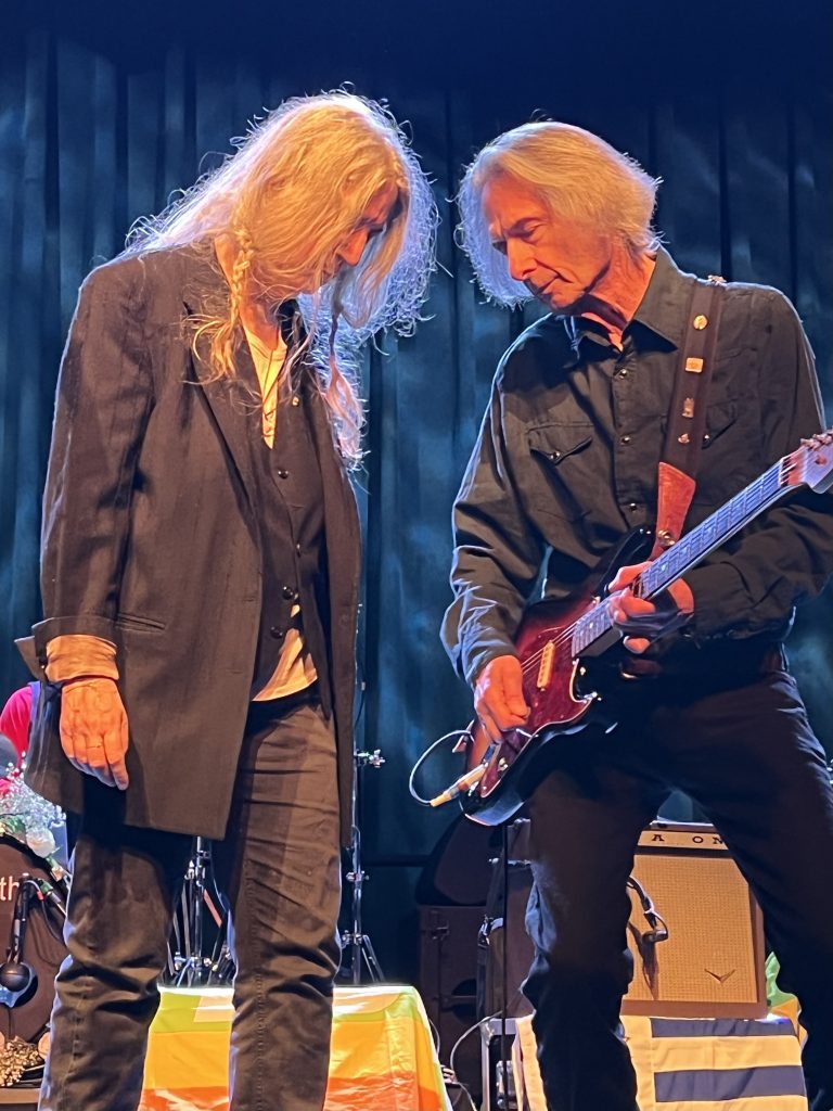 Patti Smith feiert ihren Geburtstag im Brooklyn Steel am 30. Dezember 2022. Das Bild zeigt Patti während ihrer Show auf der Bühne. Sie und Lenny Kaye stehen sich direkt gegenüber. Ihre Köpfe sind leicht nach unten geneigt, Lenny spielt dabei Gitarre.